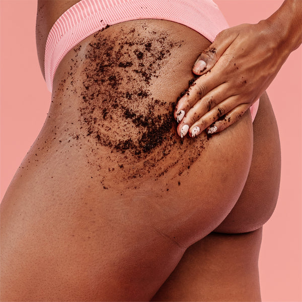 Coffee scrub from the frank body Scrub Stars Kit massaged over a hip and bum in pink underwear, with a hand working the grounds in, on a pink background.