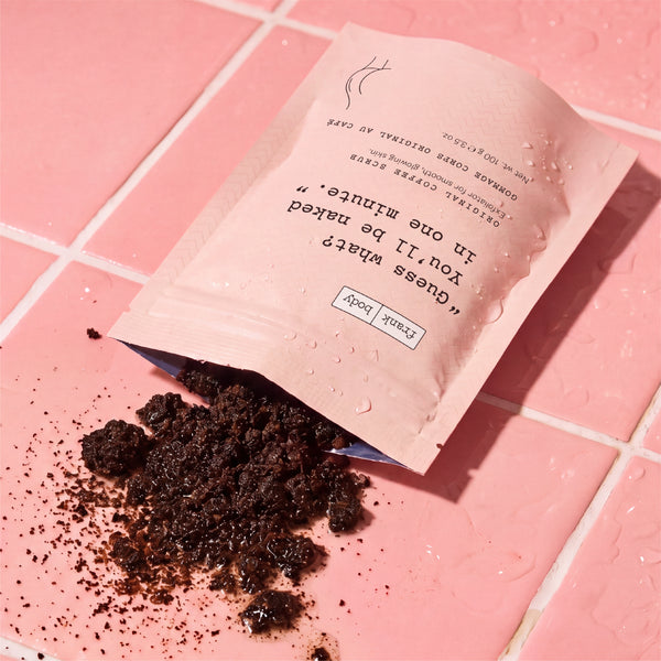 A pink resealable pouch labeled lies open on a pink tiled surface, with dark brown crumbly contents spilled out. Water droplets are visible on the pouch and background.