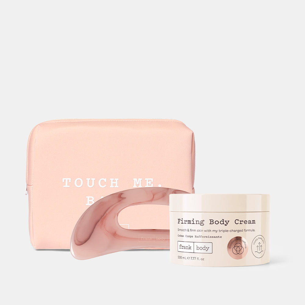 A pink silicone beauty tool with a curved handle, shown with a pale pink zip pouch and a cream-colored jar labeled 'Firming Body Cream' on a light gray background.