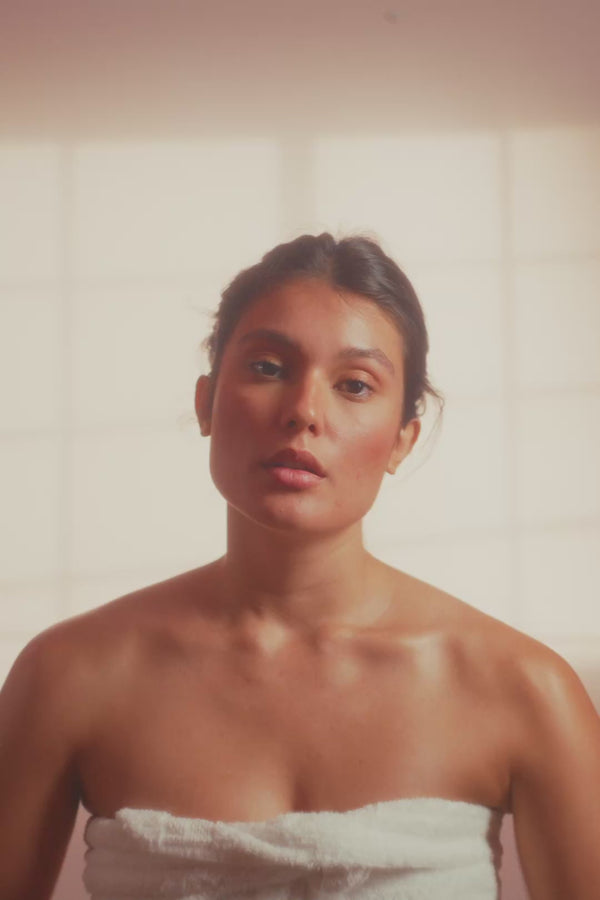 frank body Firm + Glow Tanning Jelly video: a woman wrapped in a towel in a sunlit bathroom applying the tanning jelly.
