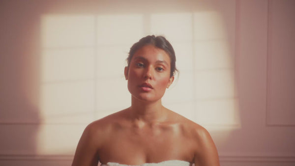 frank body Firm + Glow Tanning Jelly video: a woman wrapped in a towel in a sunlit bathroom applying the tanning jelly.
